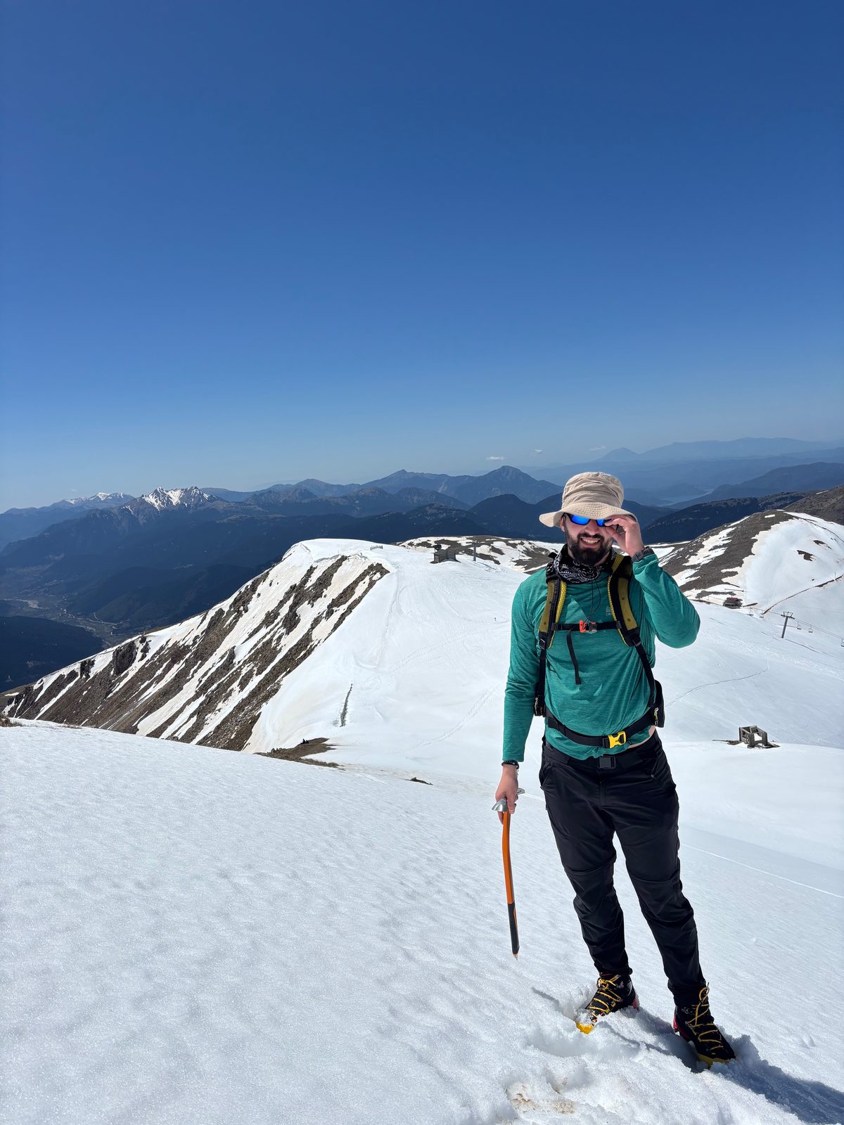 Standing on a snow-covered summit with an ice axe, ridgelines behind